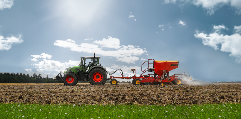 Traktor fährt auf einem Acker bei strahlendem Sonnenschein